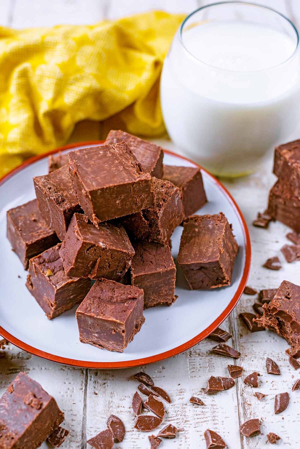 A pile of fudge cubes on a plate in front of a glass of milk.