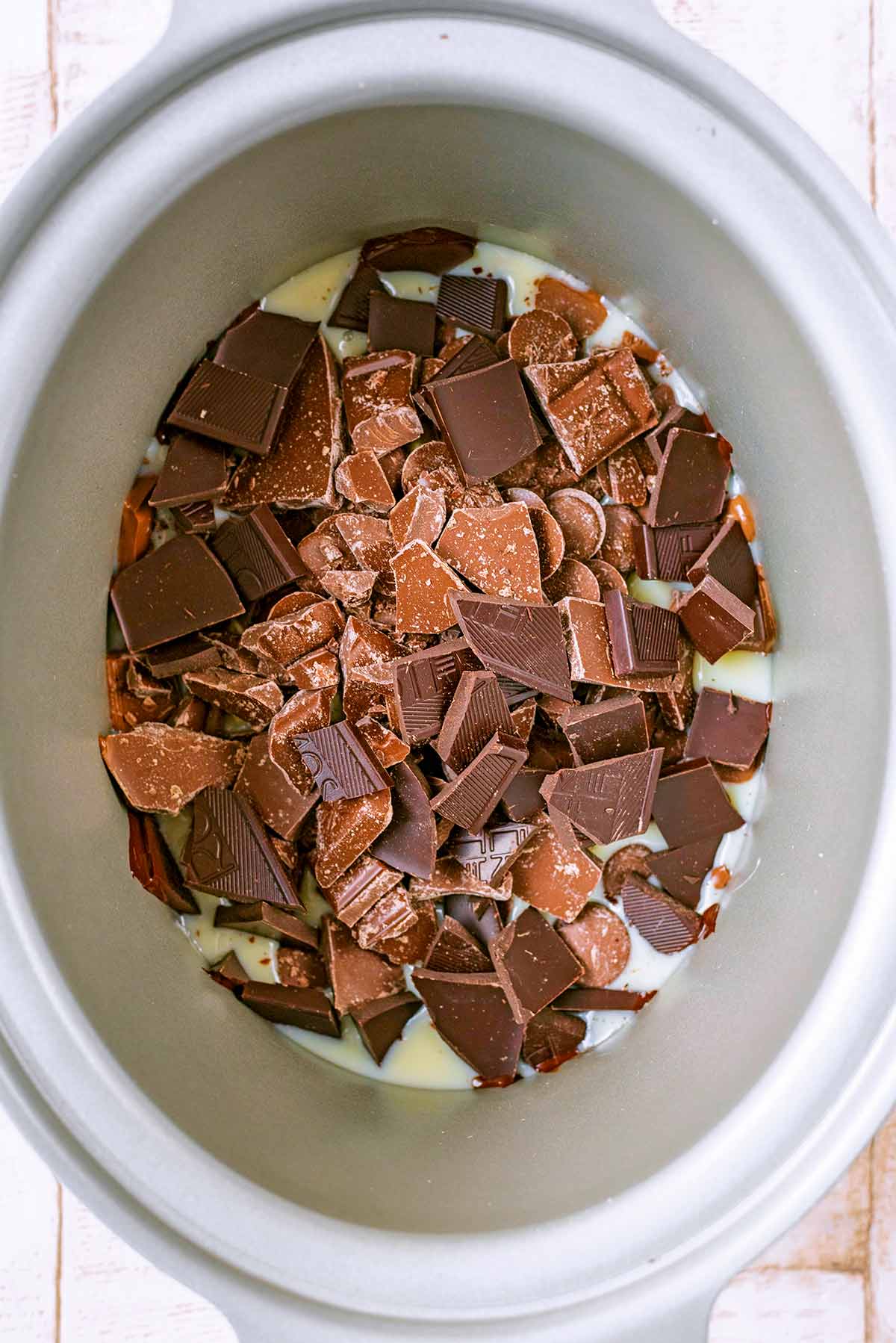 A slow cooker pot full of condensed milk and broken chocolate.