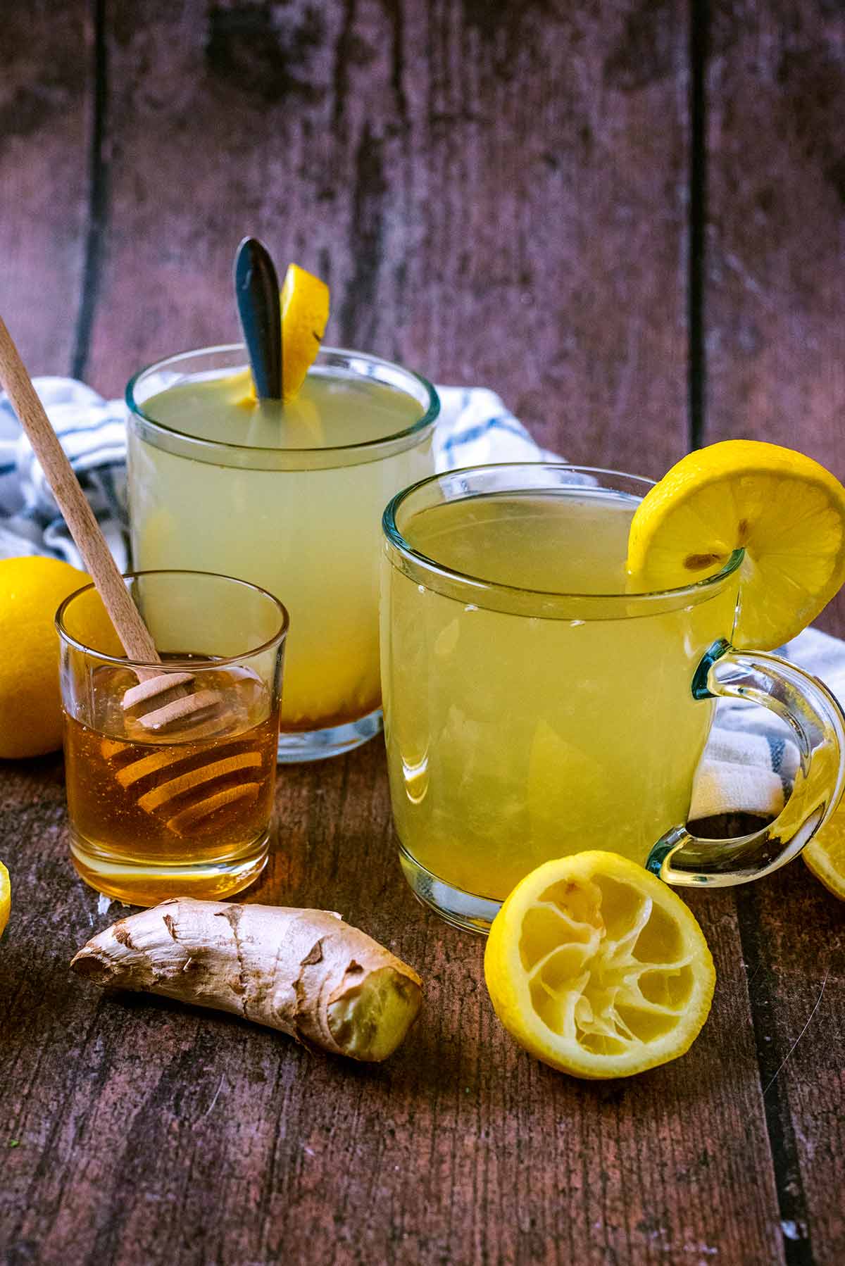 Two glasses of hot lemon and honey on a wooden surface.