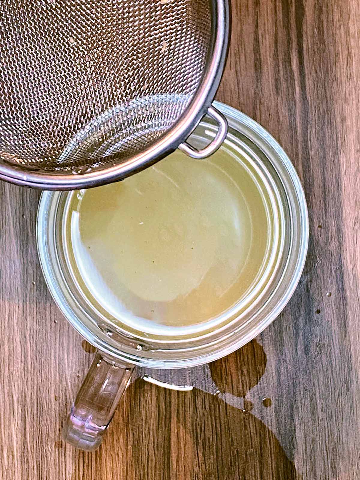 A fine sieve held over a a glass with ginger water strained through it.