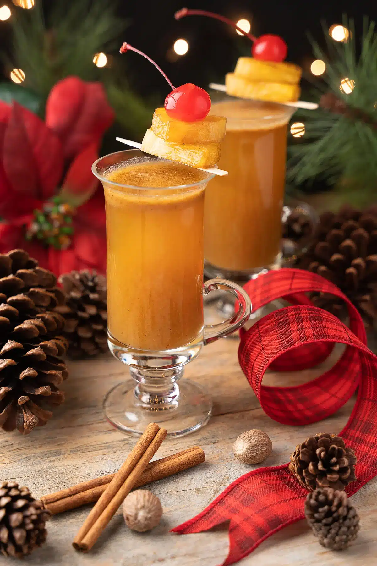 Two tall glasses of dark orange drink topped with pineapple chunks and a cherry.