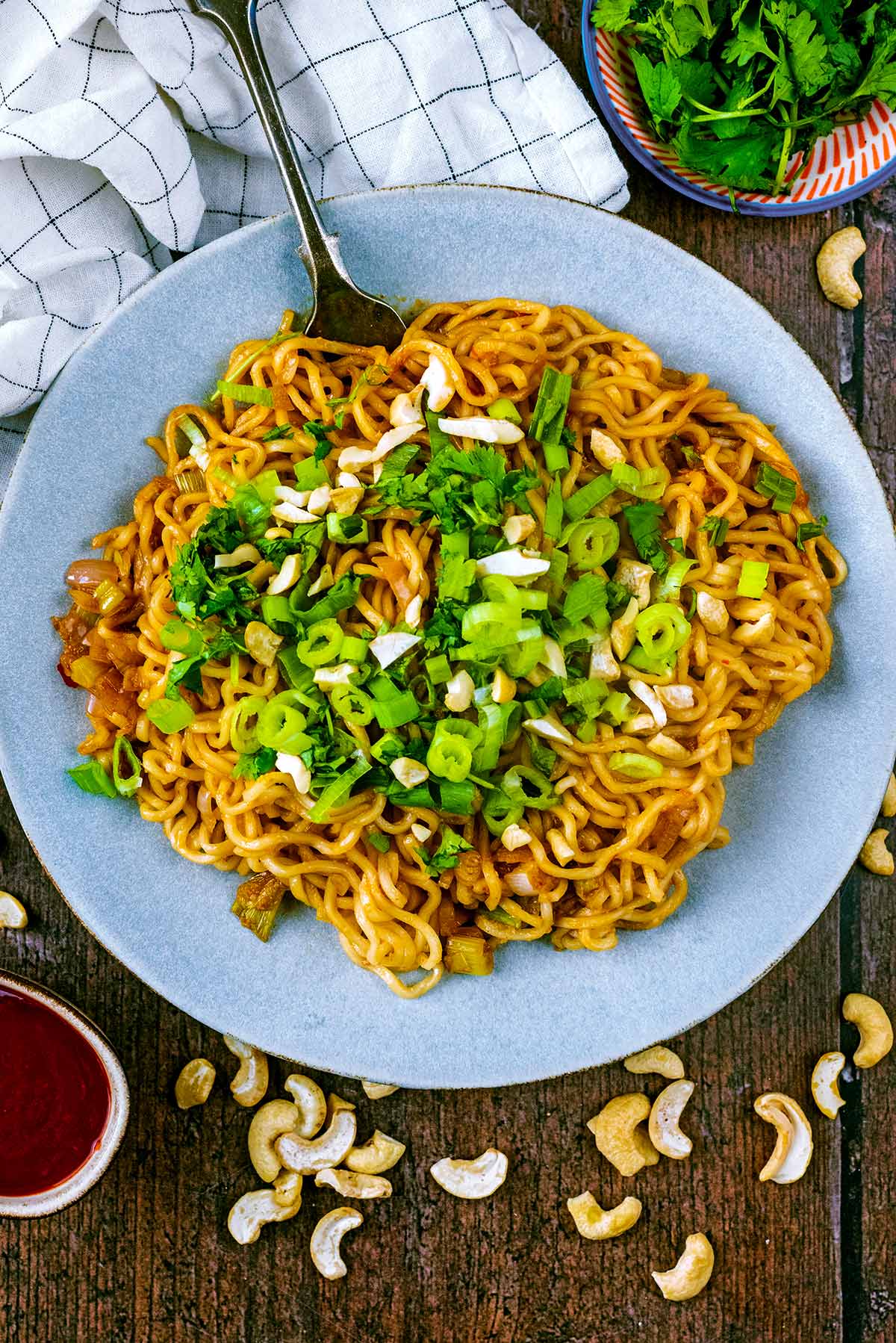A plate of noodles topped with sliced spring onion and chopped cashews.