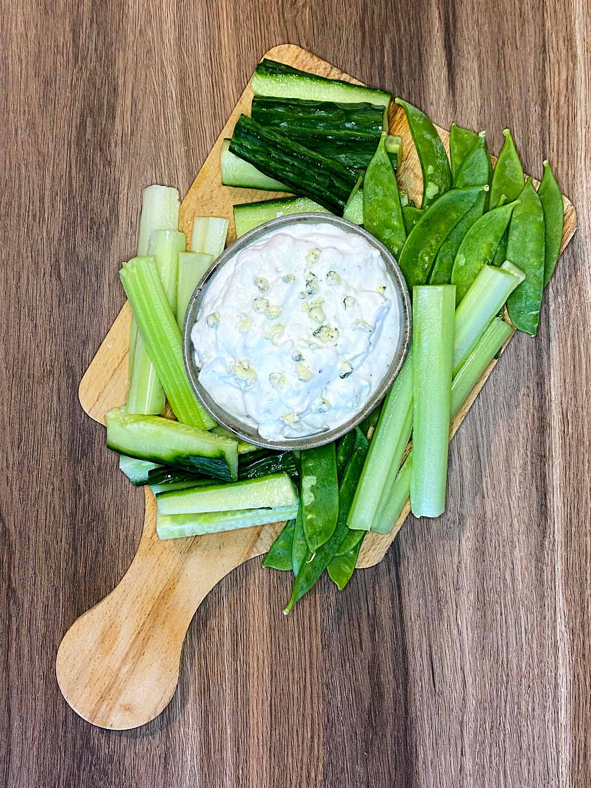 Cheese dip on a board surrounded by green crudités.
