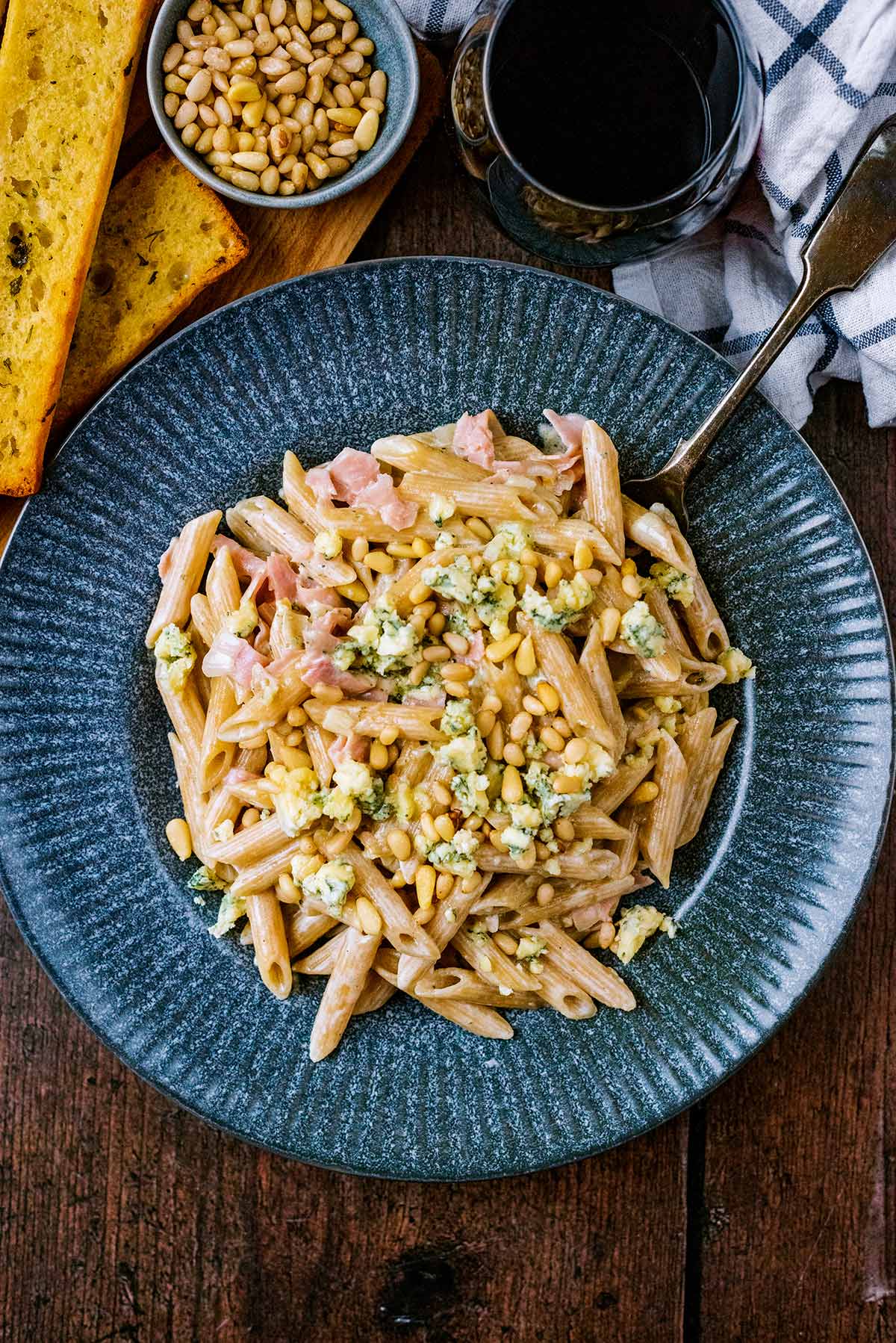 A plate of creamy pasta topped next to some garlic bread and a bowl of pine nuts.