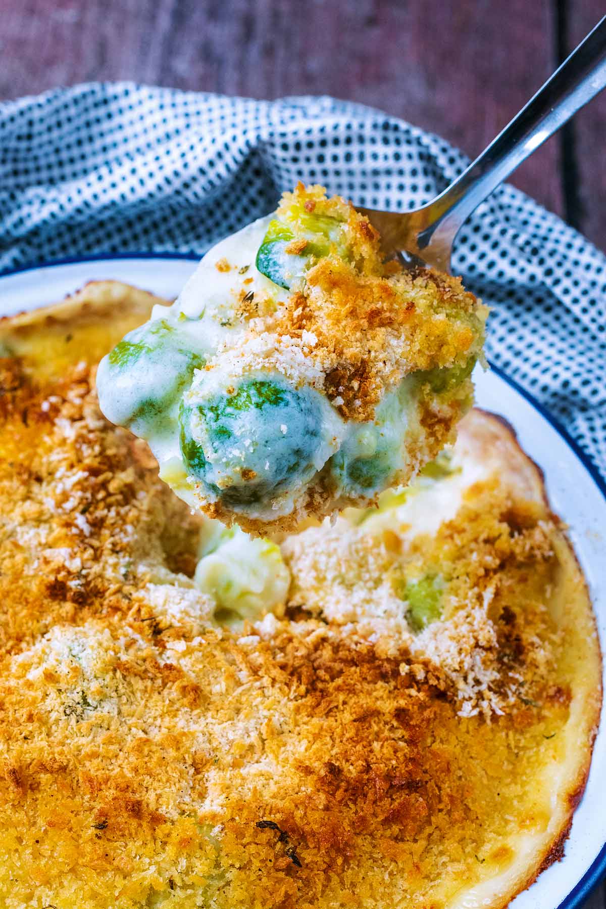 A spoon lifting up some sprout gratin from a dish.