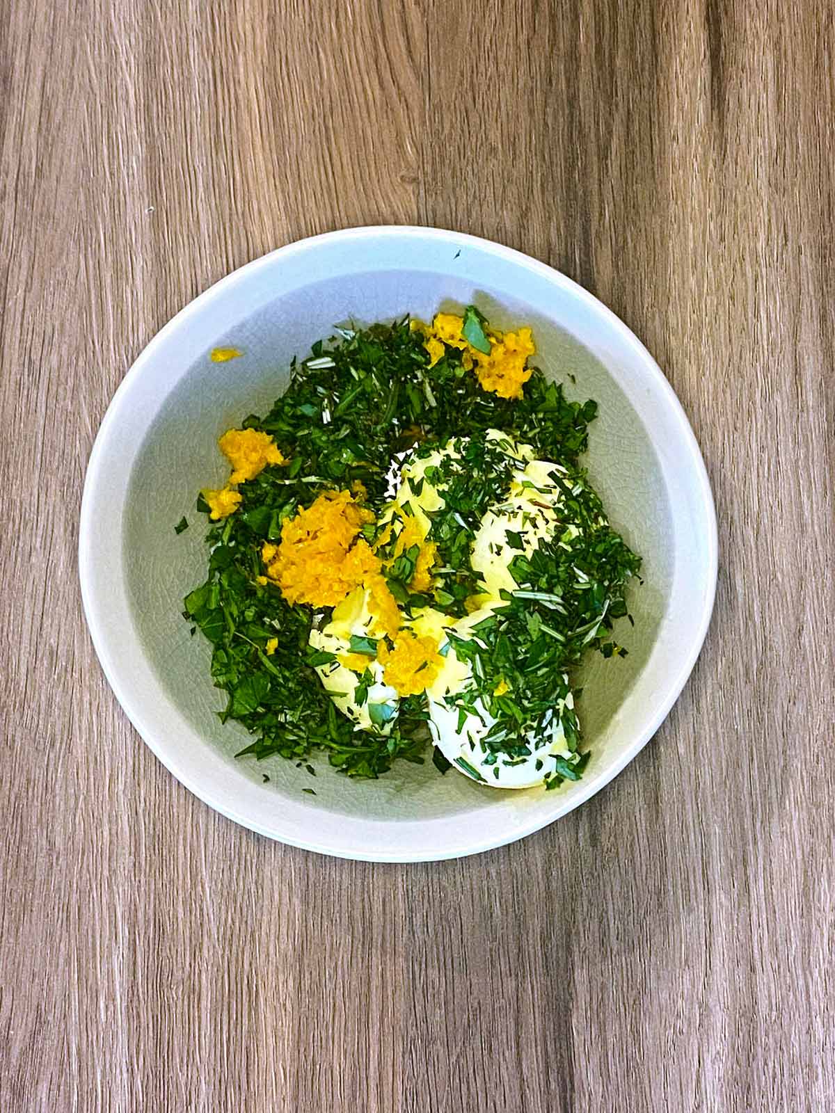 A bowl with butter, chopped herbs and orange zest in it.