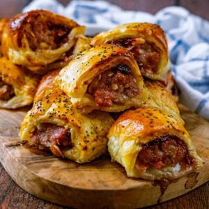 A pile of Christmas sausage rolls on a wooden board.