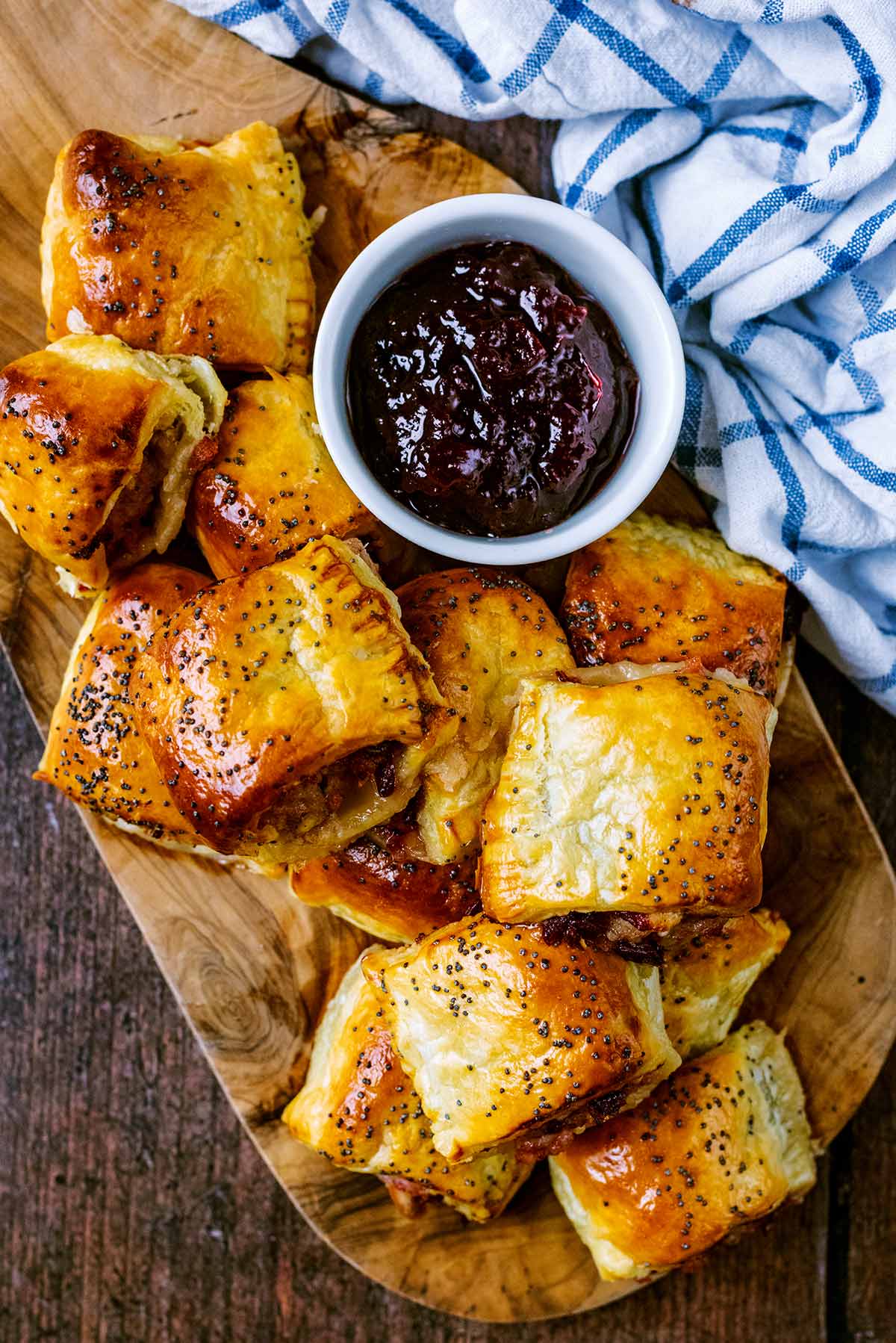 Sausage rolls on a board with a pot of cranberry sauce.