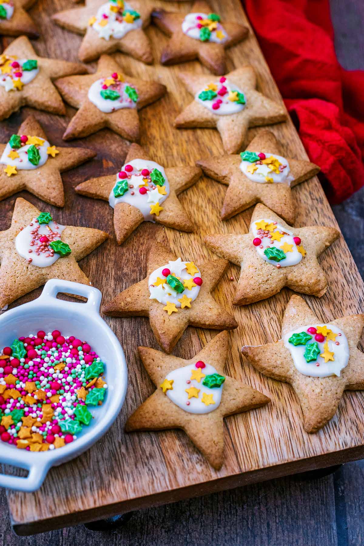 Star biscuits on a board wit ha small pot of Christmas sprinkles.