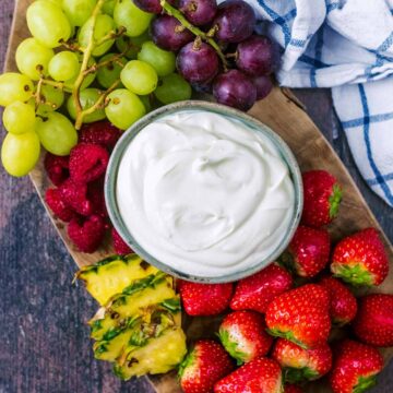 A bowl of cream cheese fruit dip on a board with a variety of fruit.