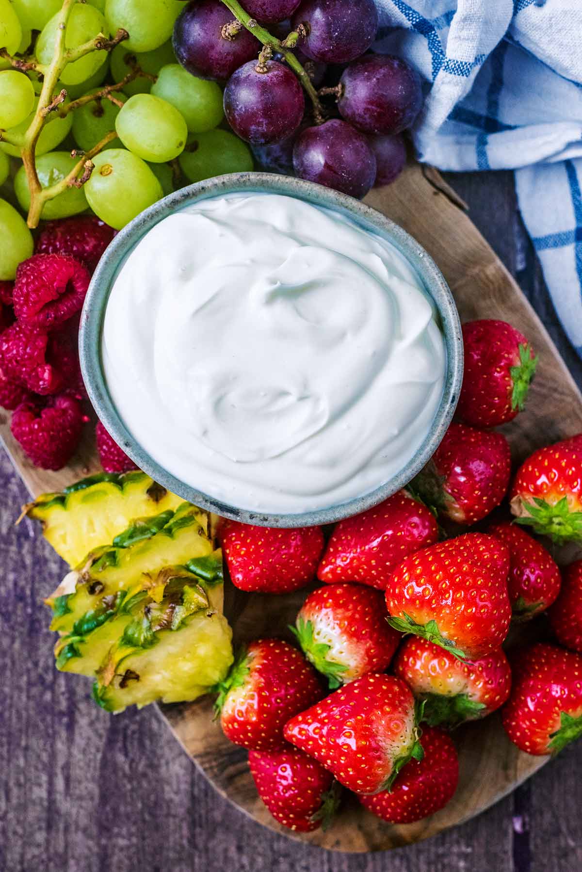 A bowl of creamy dip surrounded by grapes, strawberries, raspberries and pineapple slices.