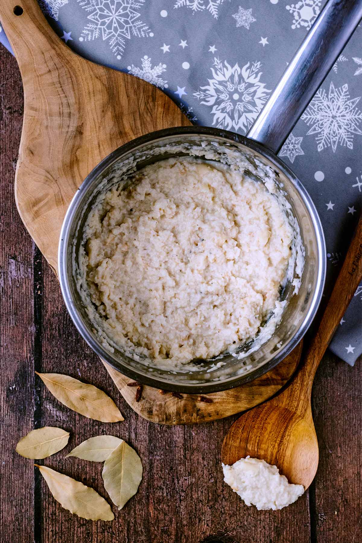 A pan of bread sauce on a board next to some bay leaves.