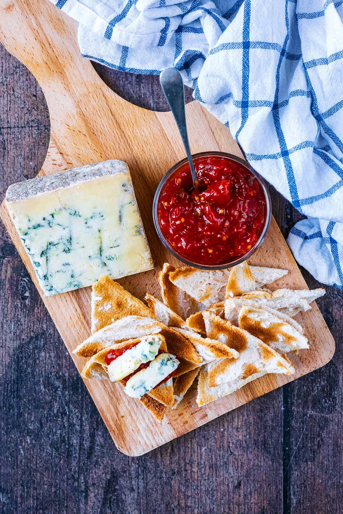 A serving board with toast triangles, blue cheese and a bowl of chutney.