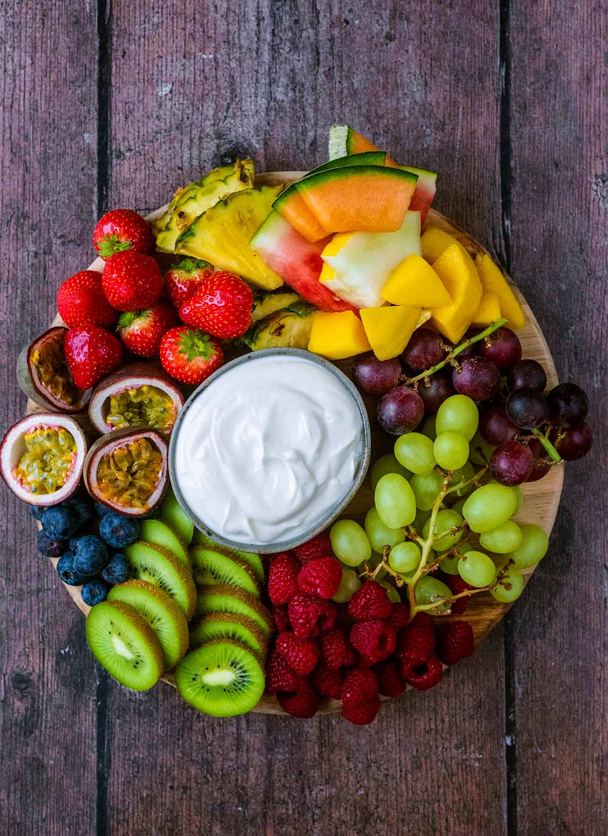 A large round platter of different fruit with a bowl of creamy dip.