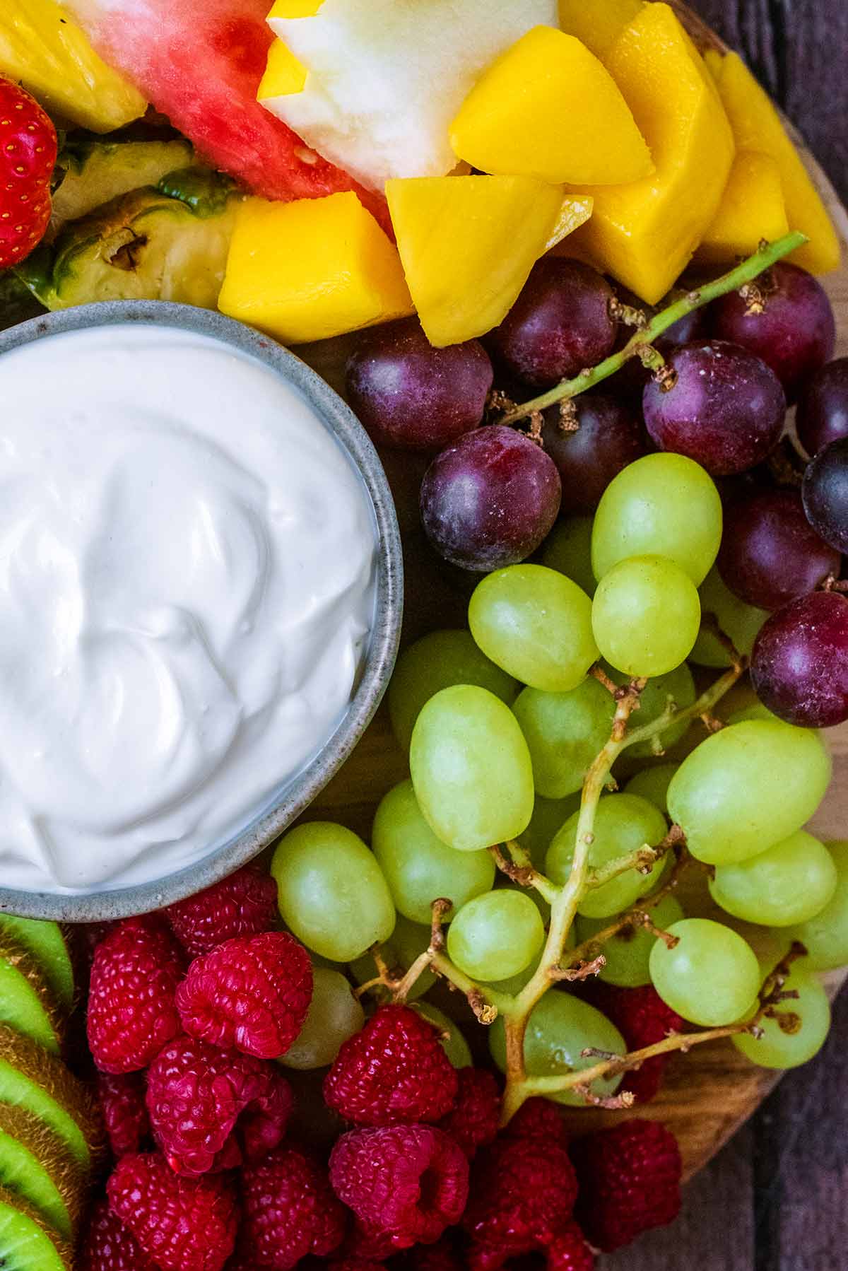 Red and green grapes, raspberries and sliced kiwi next to a bowl of creamy dip.
