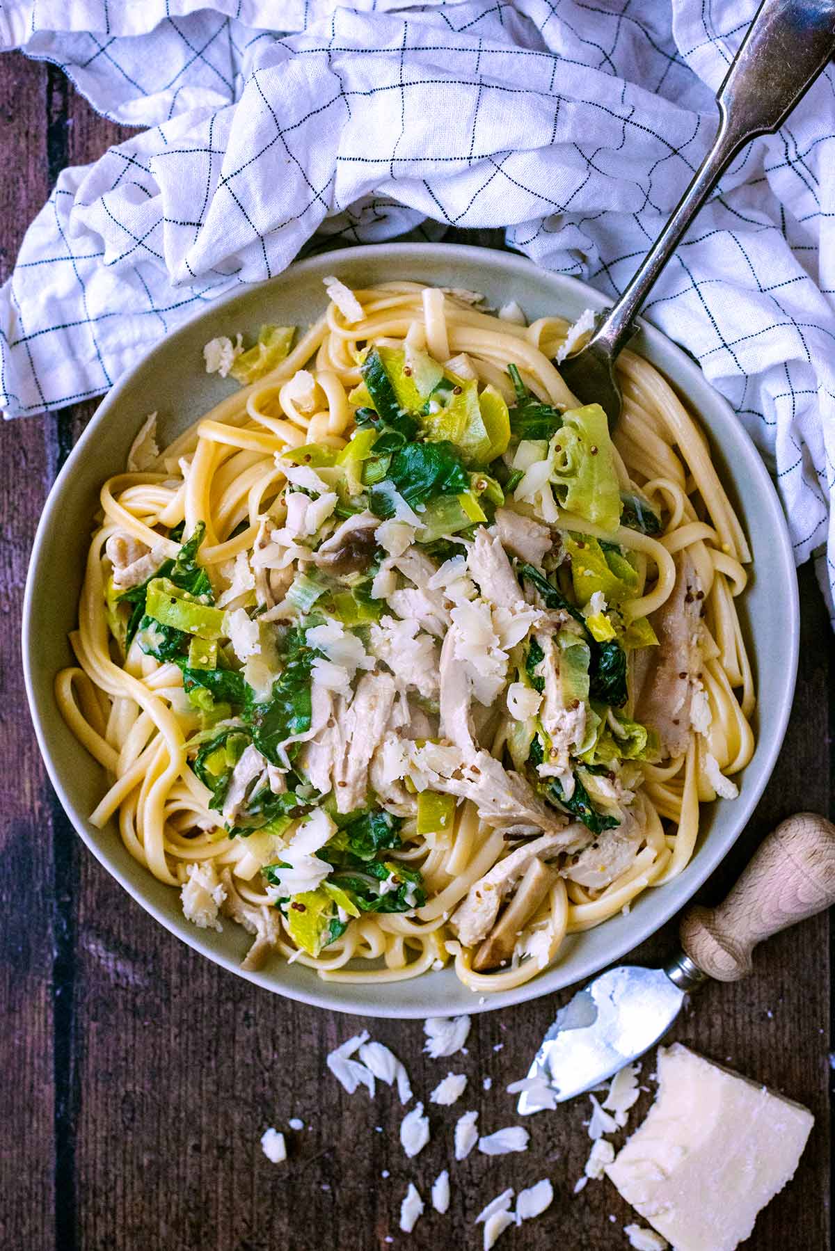 A bowl of turkey pasta next to a towel and a block of Parmesan.