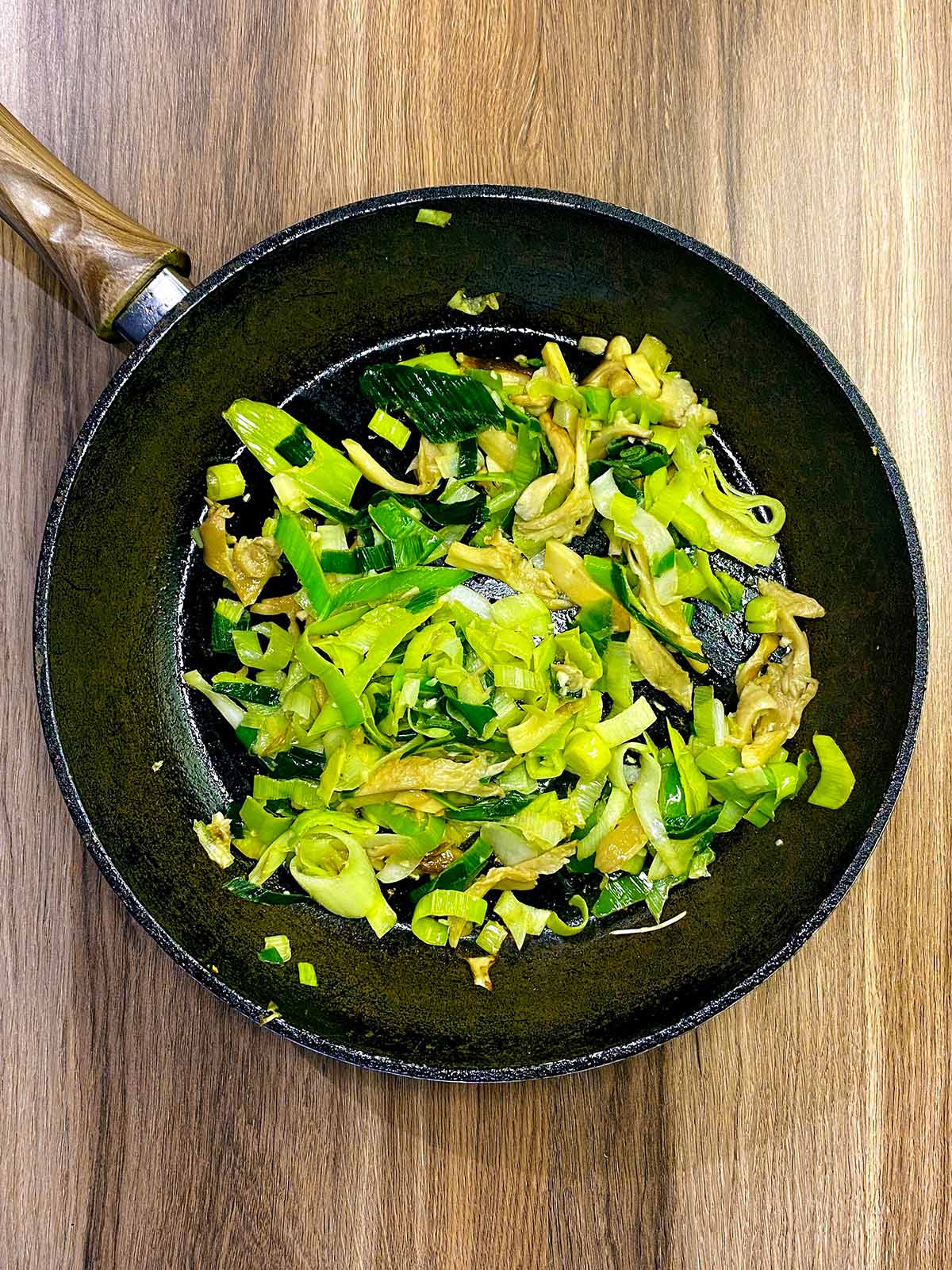 Chopped leeks and sliced mushrooms cooking in a pan.