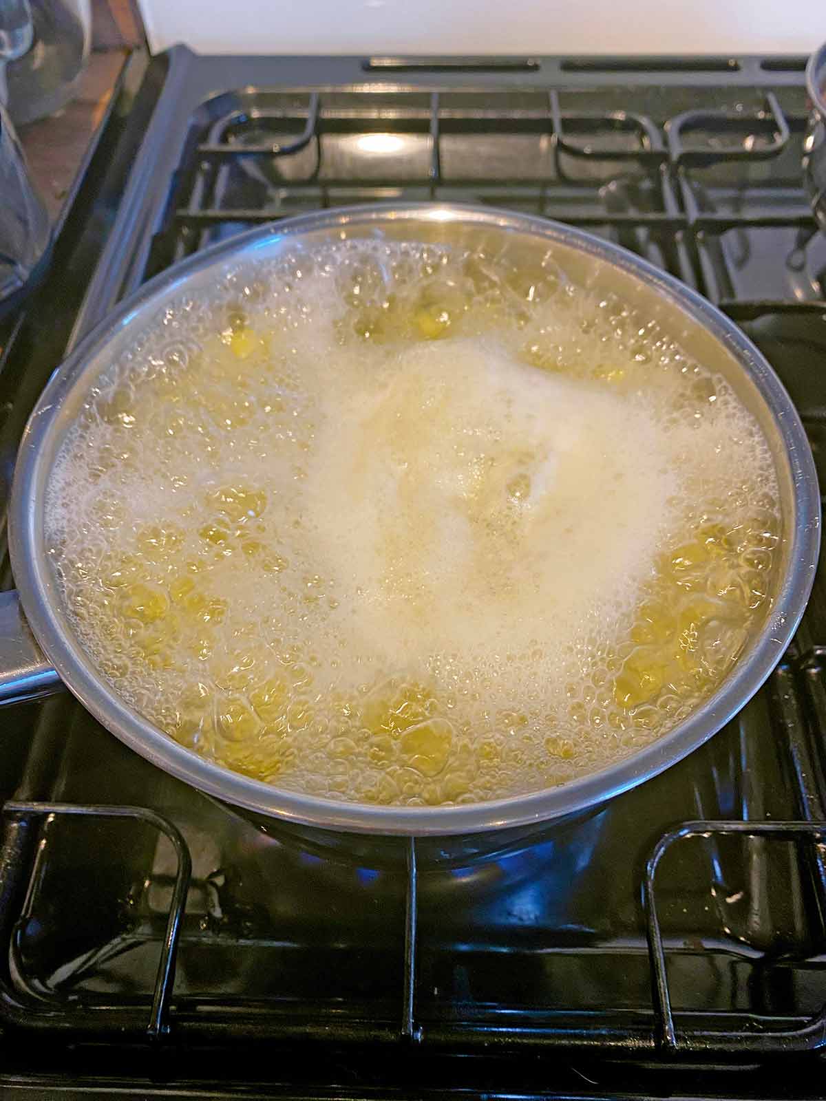 Potatoes boiling in a pan on a hob.