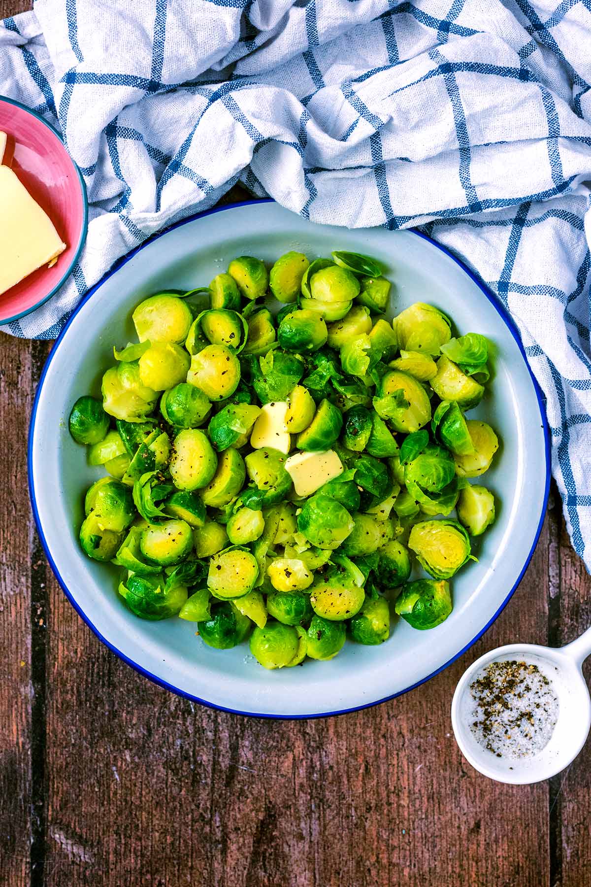 A bowl of cooked Brussels sprouts next to a checked towel.