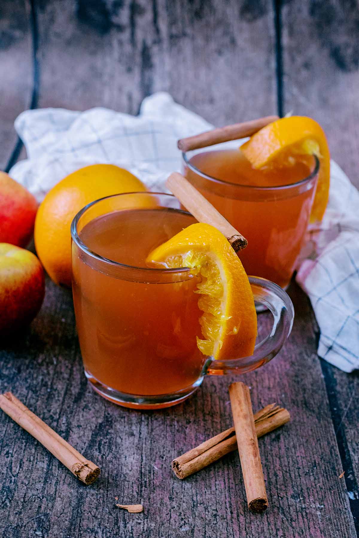 Two glasses of mulled cider next to some oranges and cinnamon sticks.