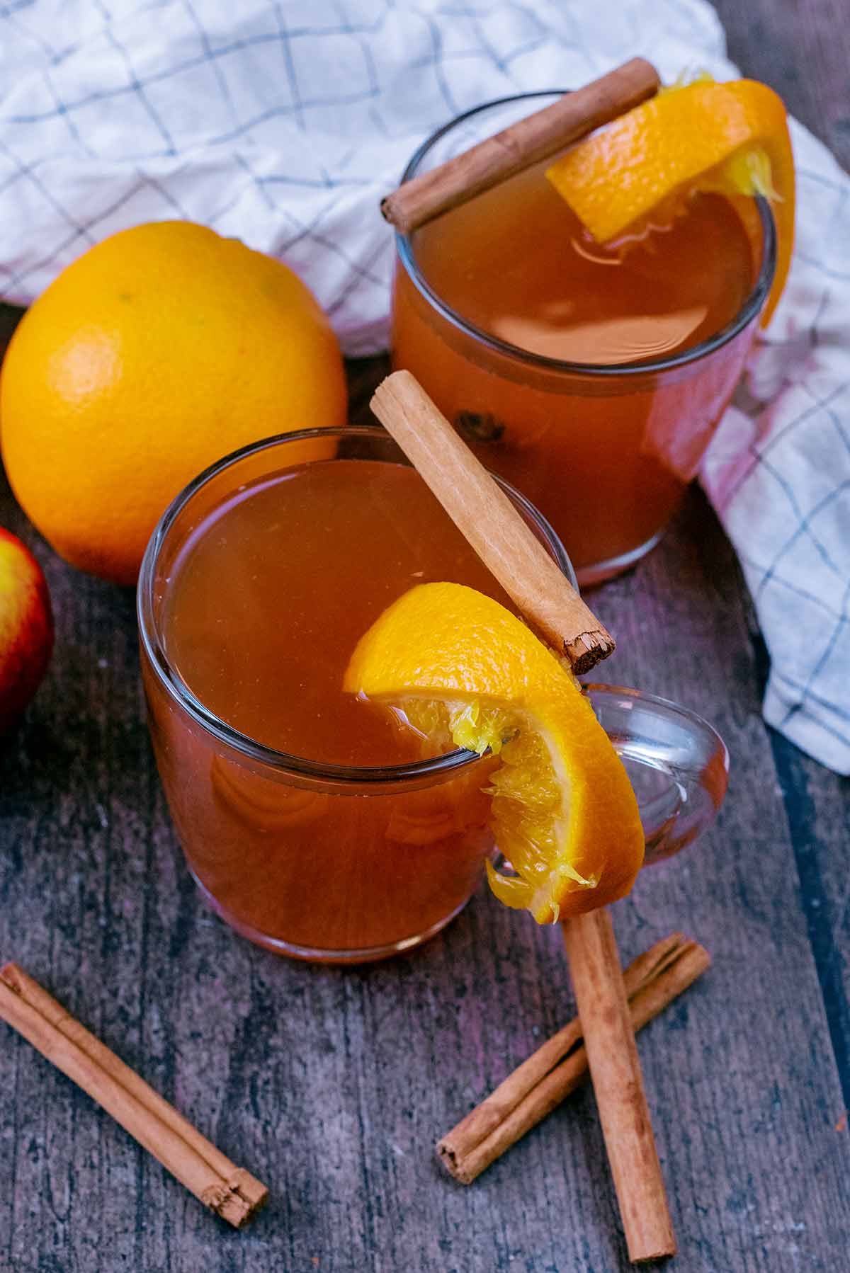 Cinnamon stick and a sliced orange on top of a glass of mulled cider.