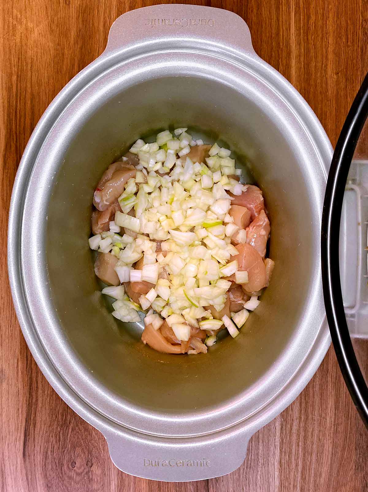 Chopped chicken breast and chopped onion in a slow cooker.