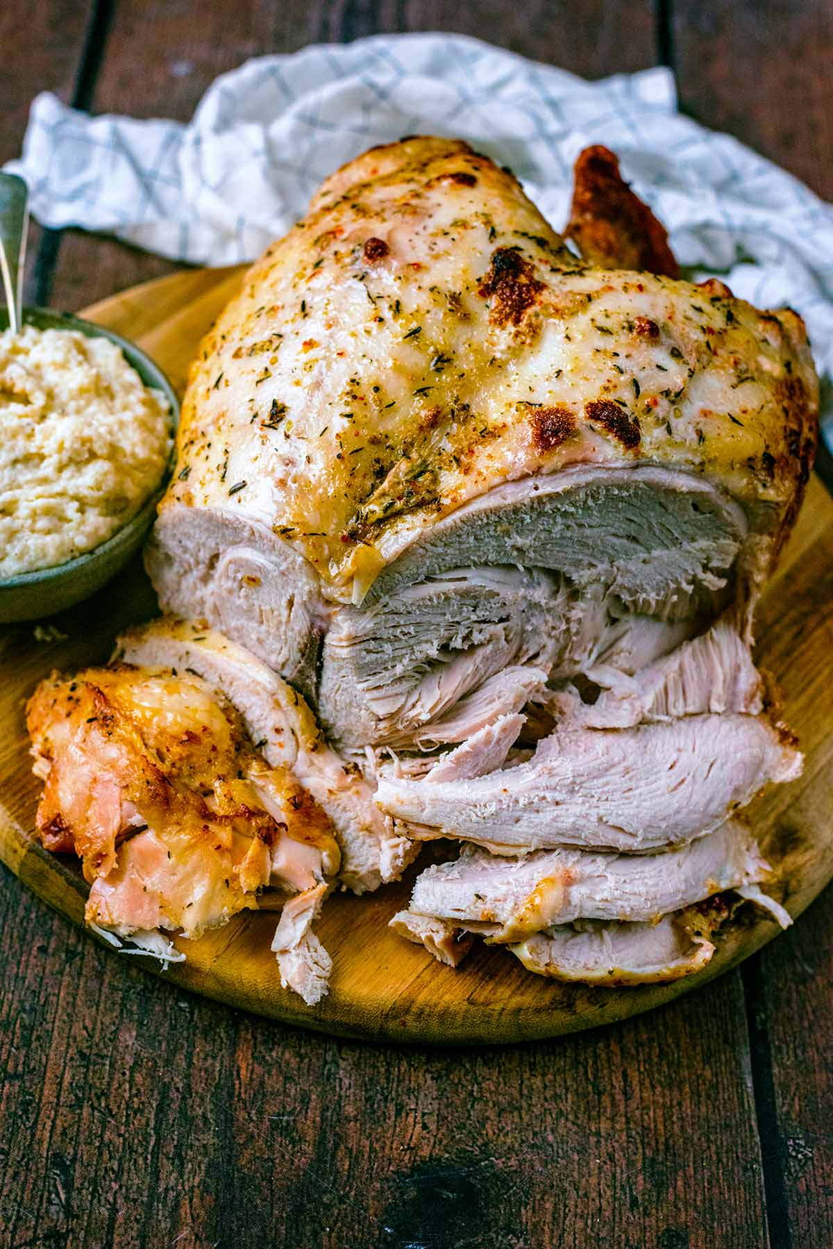 A cooked turkey crown on a wooden board with slices cut off.