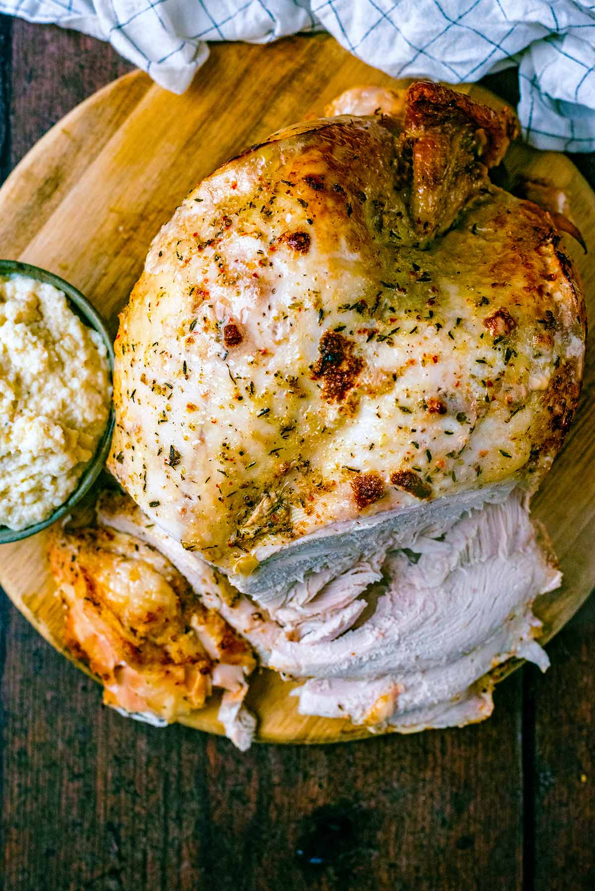 A cooked turkey crown on a board with a small bowl of bread sauce.