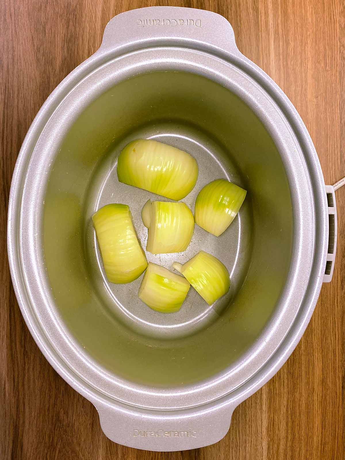 Onion halves sat in the bottom of a slow cooker bowl.
