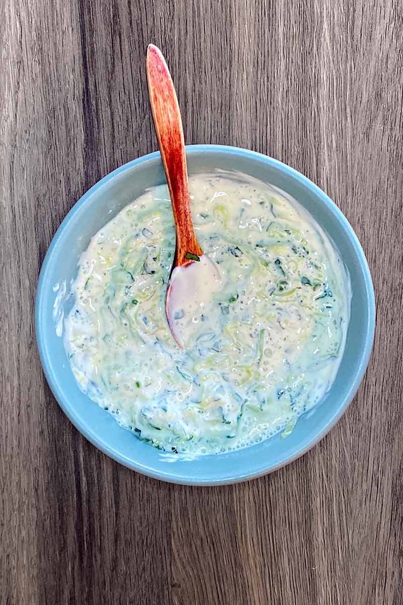 A bowl of tzatziki with a small wooden spoon in it.