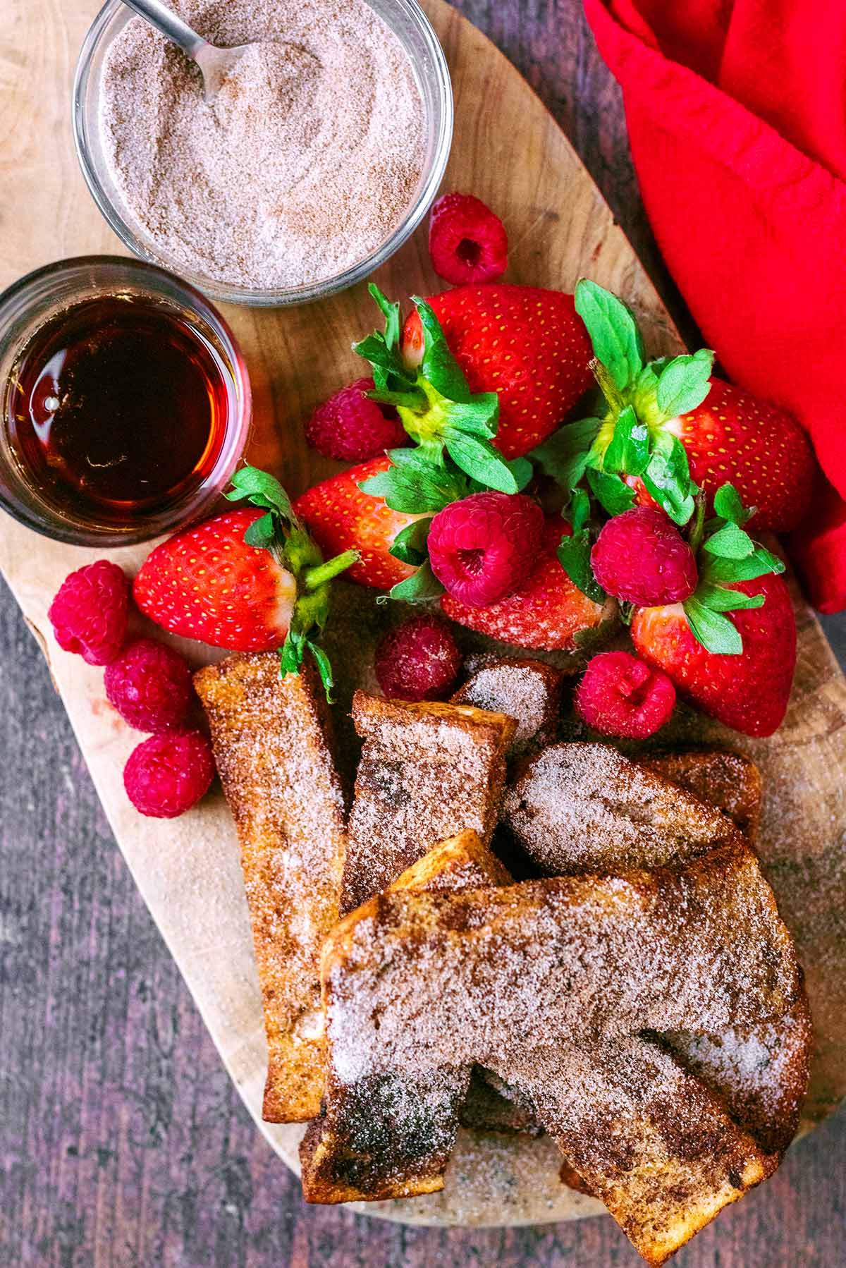 Sugar topped french toast on a board with strawberries and raspberries.