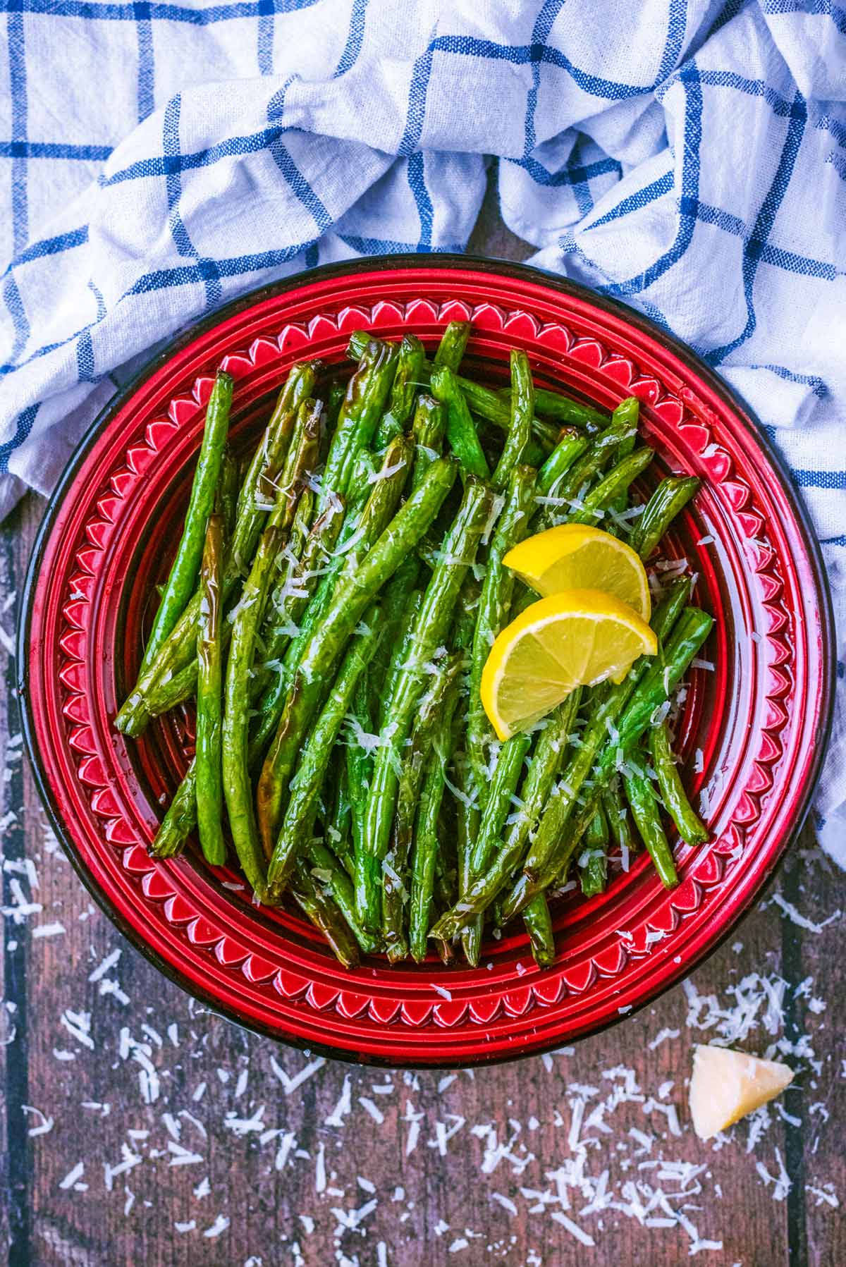 A bowl of cooked green beans with two lemon slices on top of them.