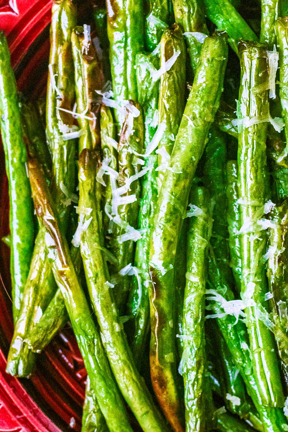Cooked green beans with grated Parmesan melting on them.