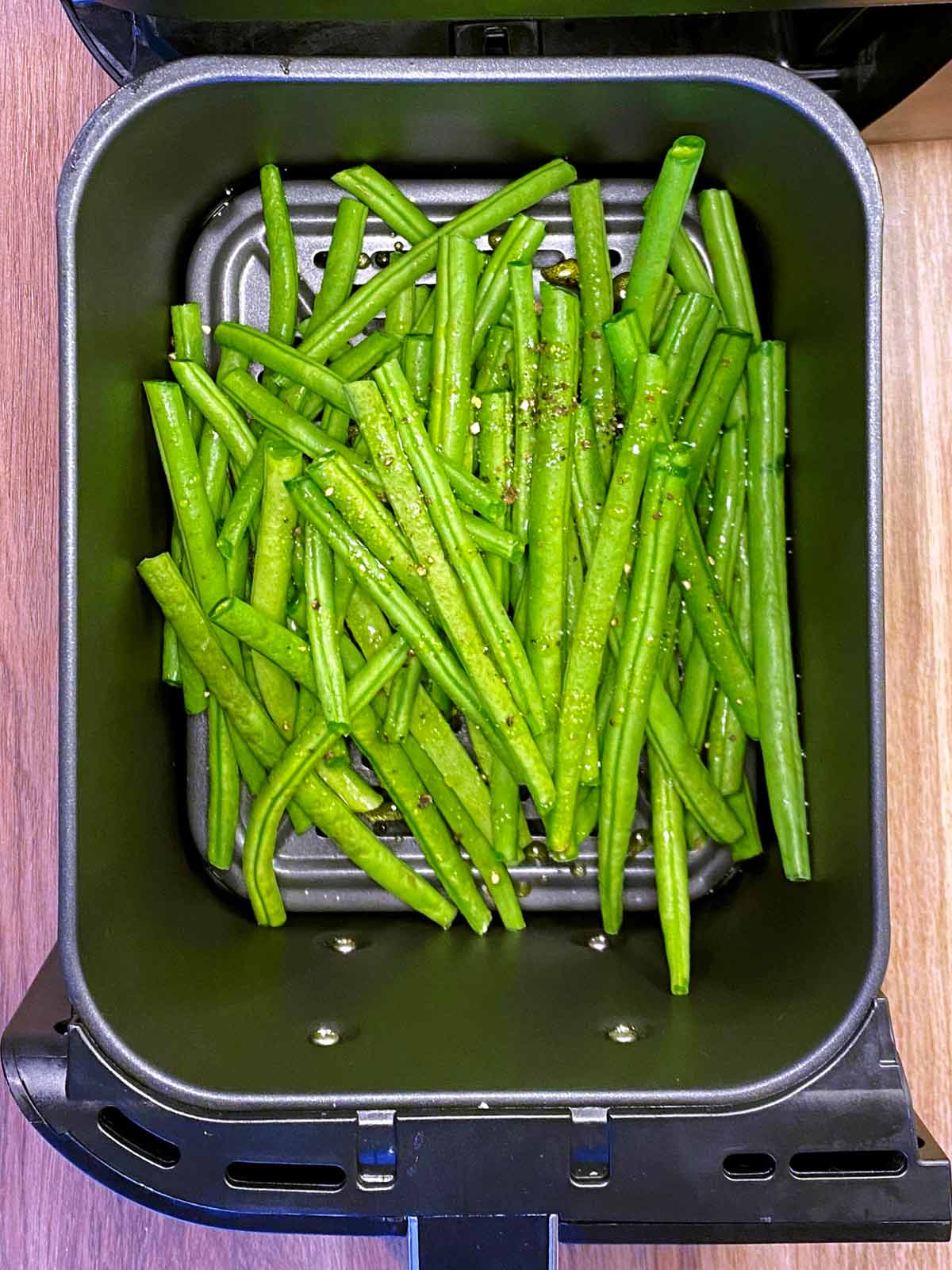 An air fryer basket with raw green beans in it.