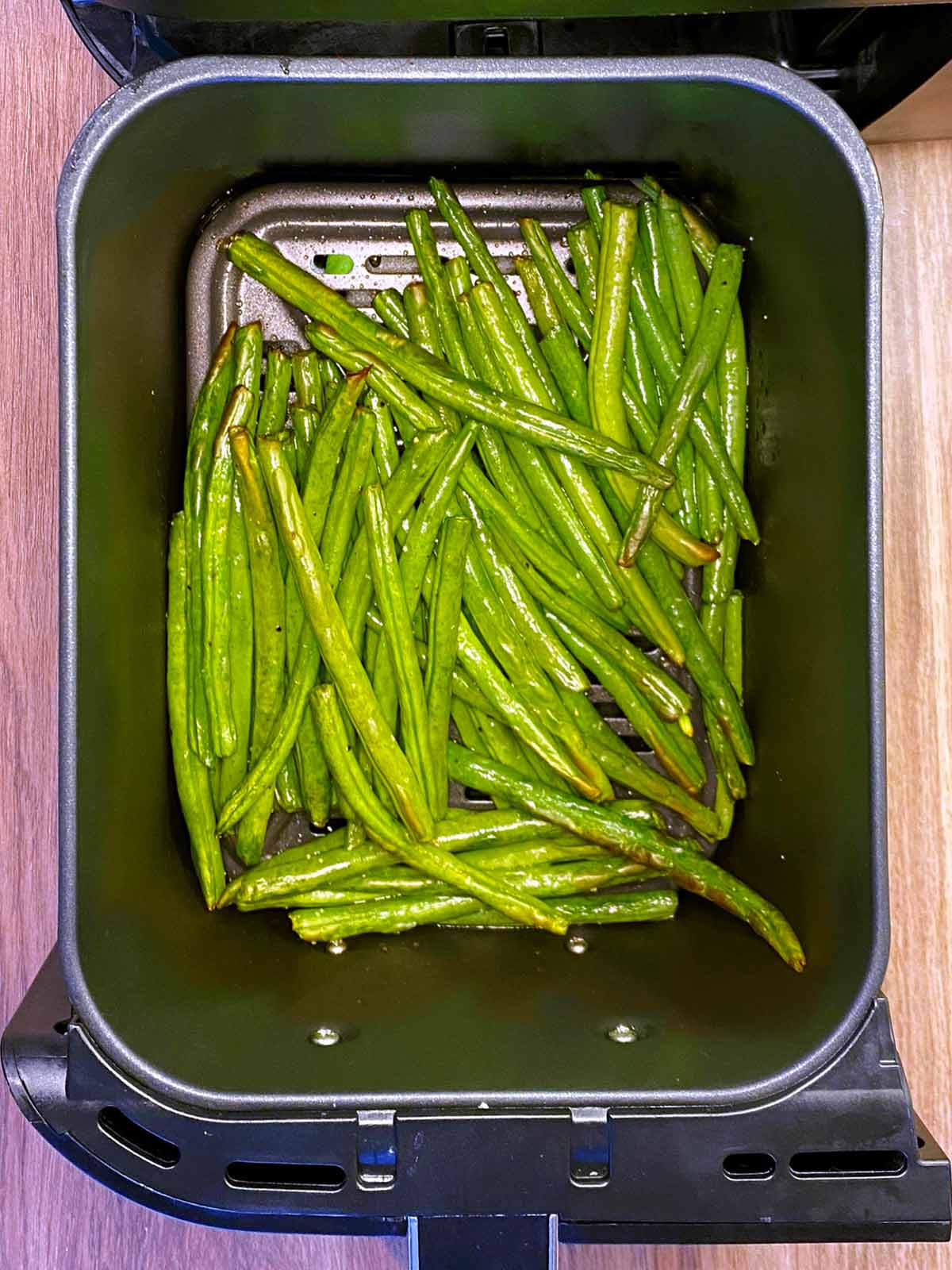 Cooked green beans in an air fryer basket.