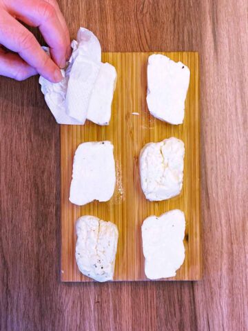 Slices of halloumi on a wooden board being patted with paper towel.