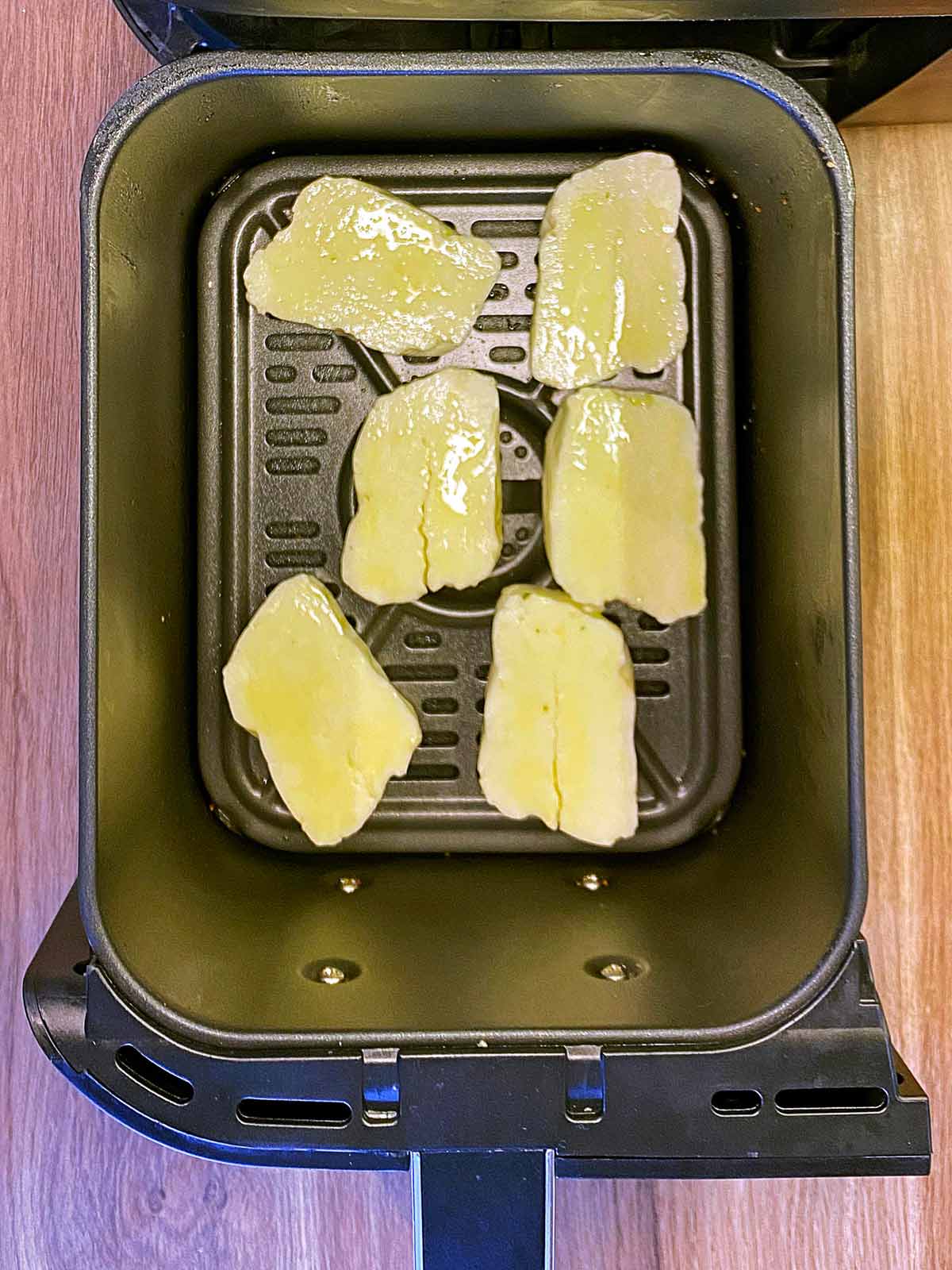 Slices of halloumi in an air fryer basket.