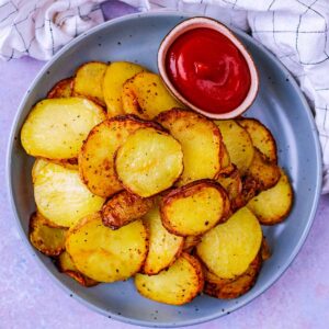 A plate of air fryer potato slices with a small pot of ketchup.