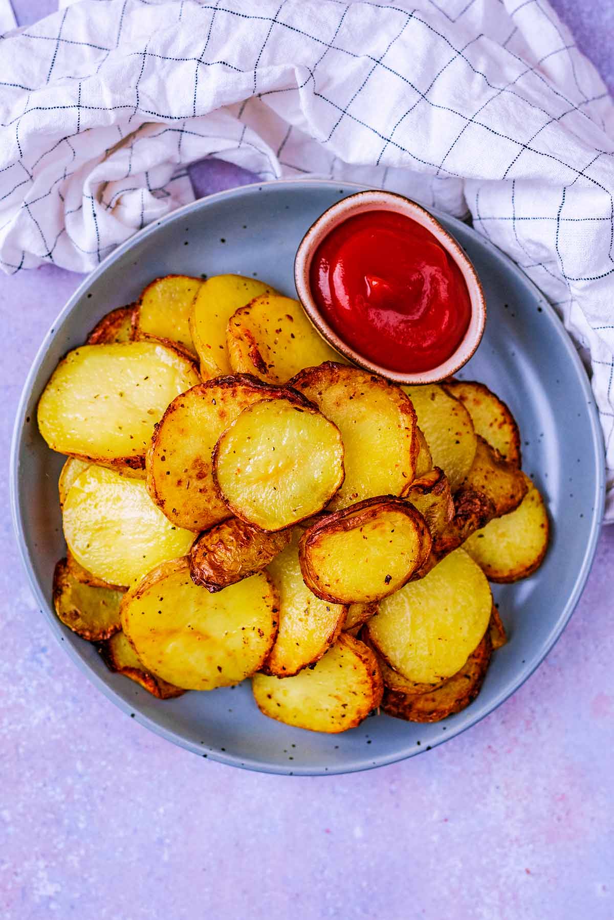 A plate of cooked sliced potatoes with some ketchup.