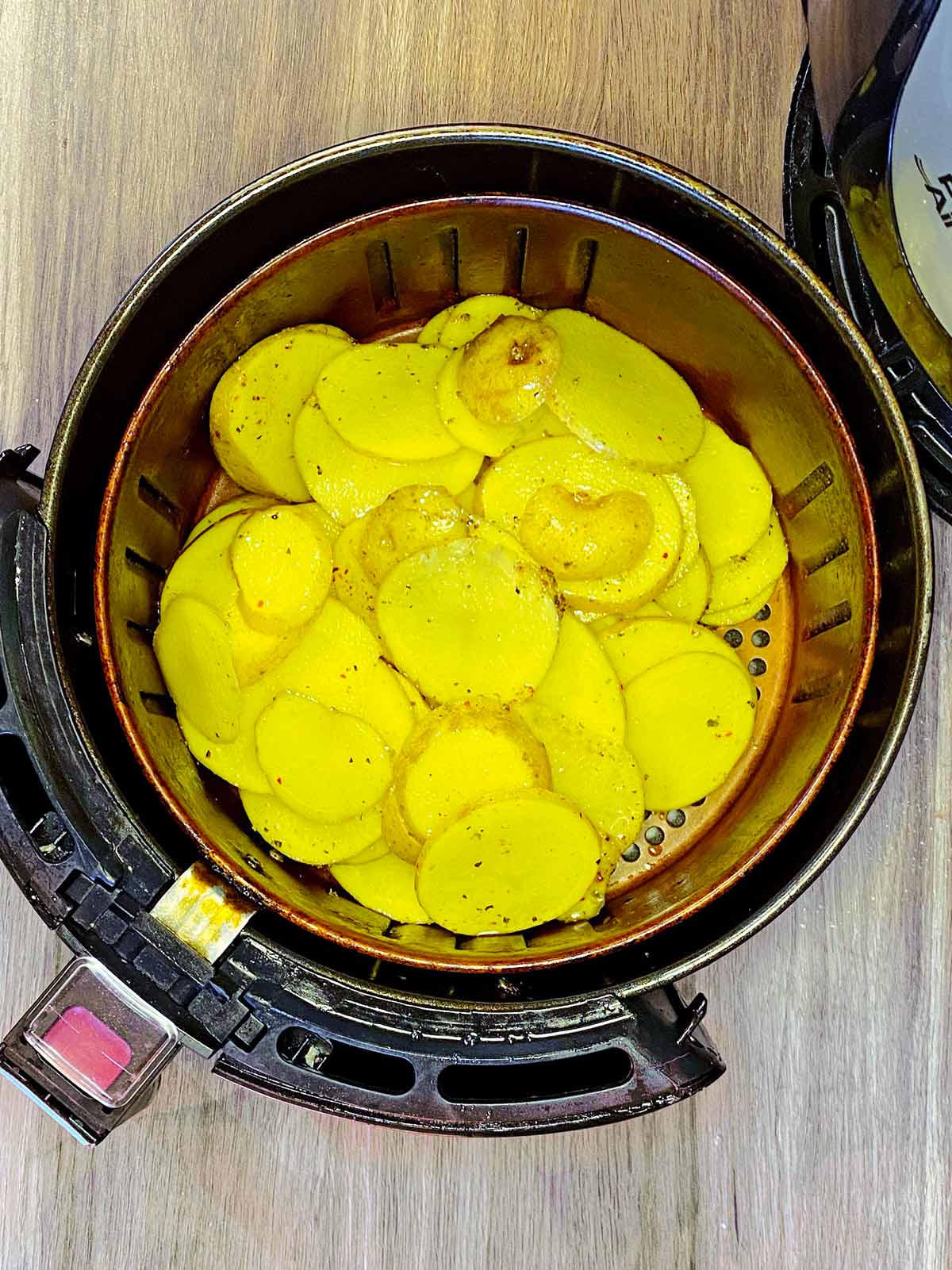 Uncooked potato slices in an air fryer basket.