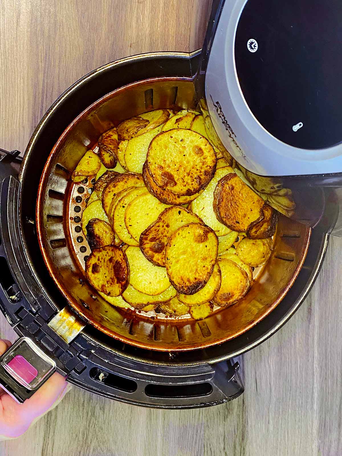 Cooked potato slices being removed from an air fryer.