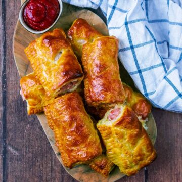A pile of air fryer sausage rolls on a wooden board.