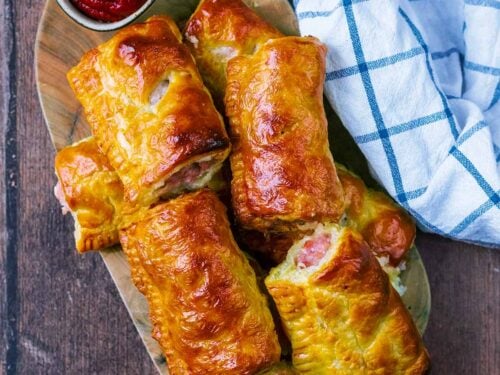 A pile of air fryer sausage rolls on a wooden board.