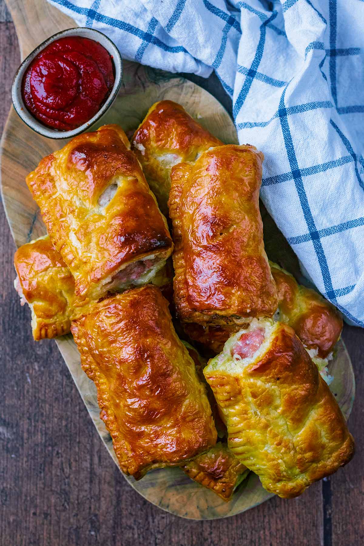 Eight sausage rolls on a board with a small bowl of ketchup.