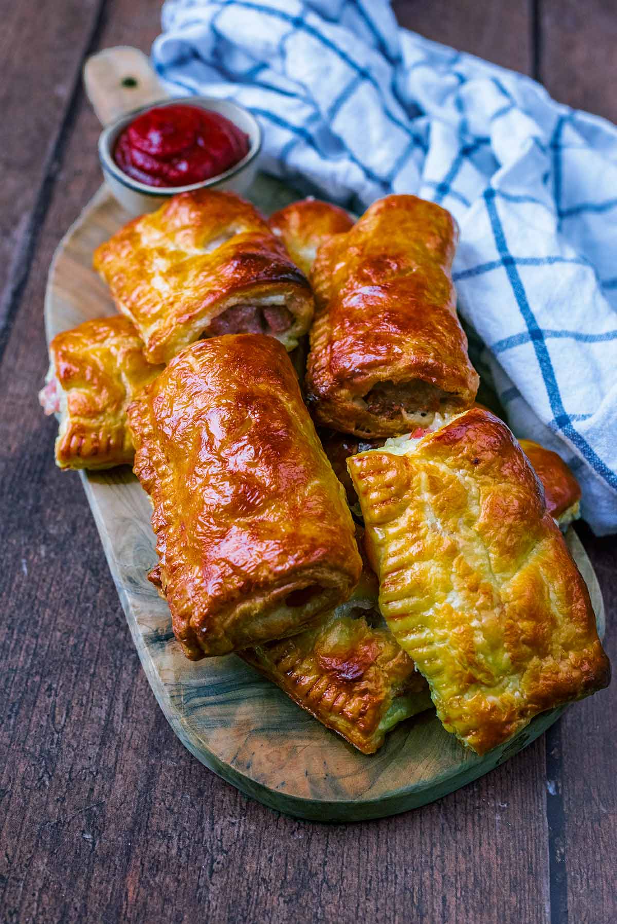 Sausage rolls on a wooden board in front of a checked towel.