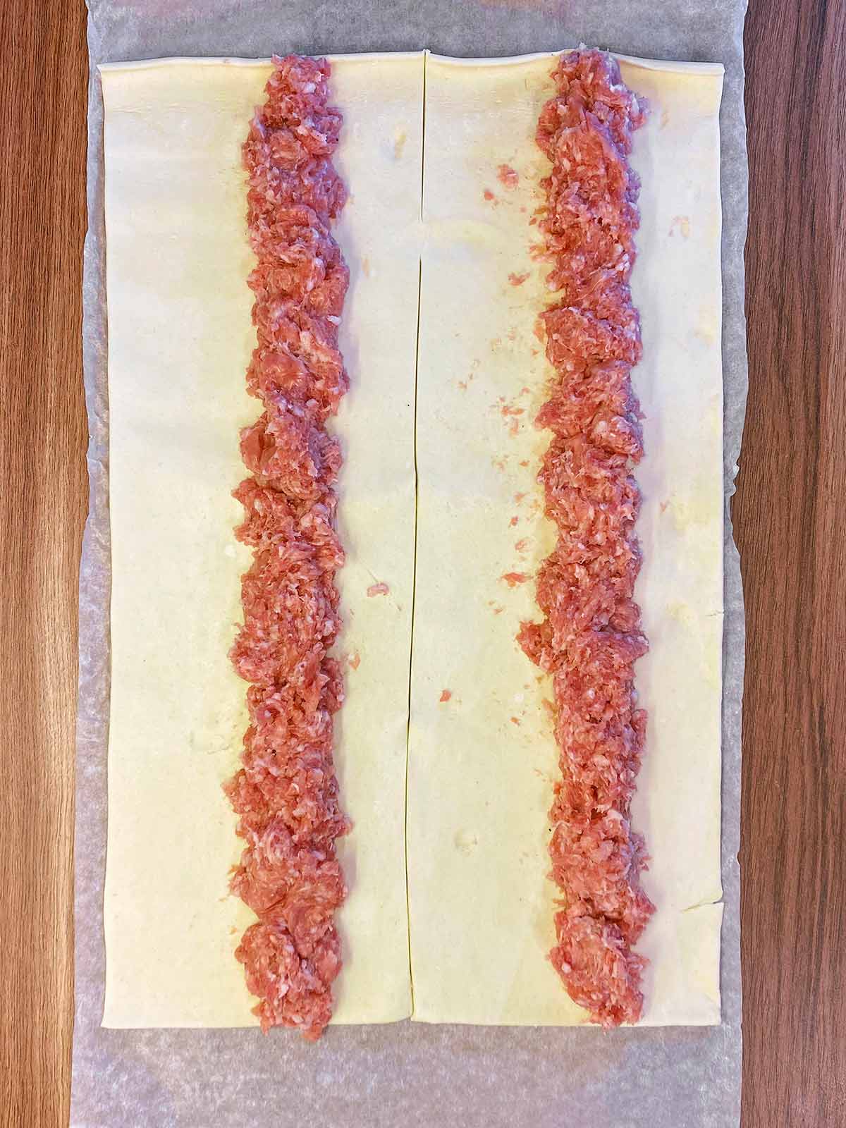 A sheet of pastry with two lines of sausage meat on it.
