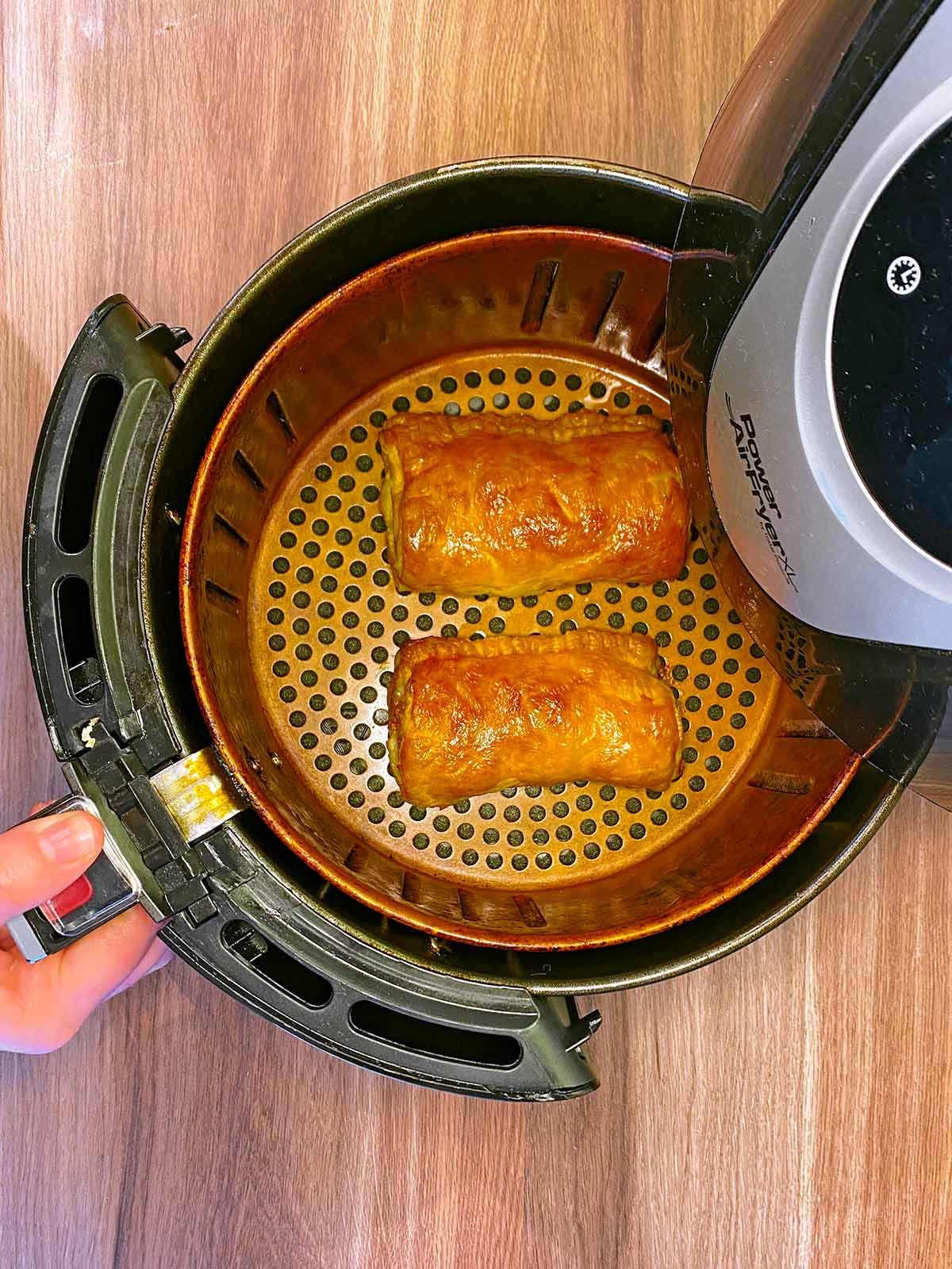 Two cooked sausage rolls in an air fryer basket.