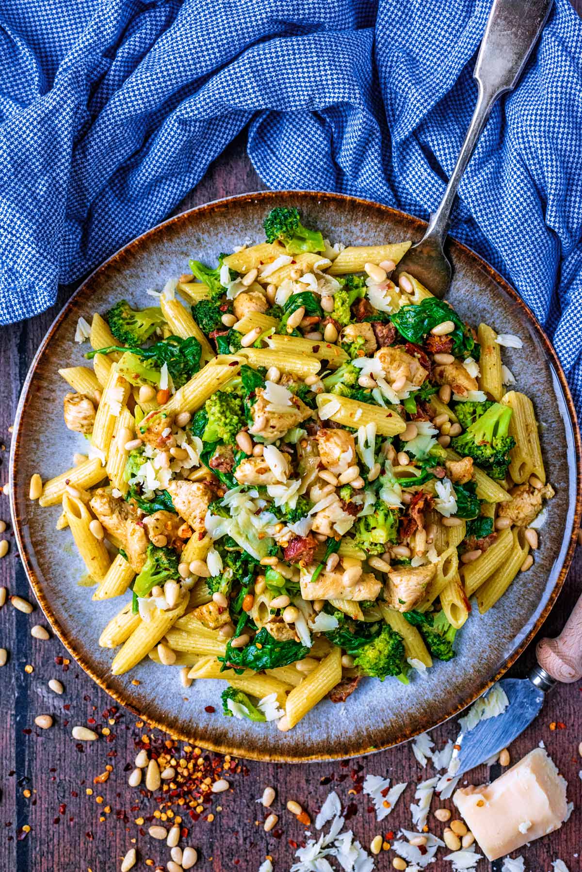 A plate of chicken and vegetable pasta next to a towel and some cheese.