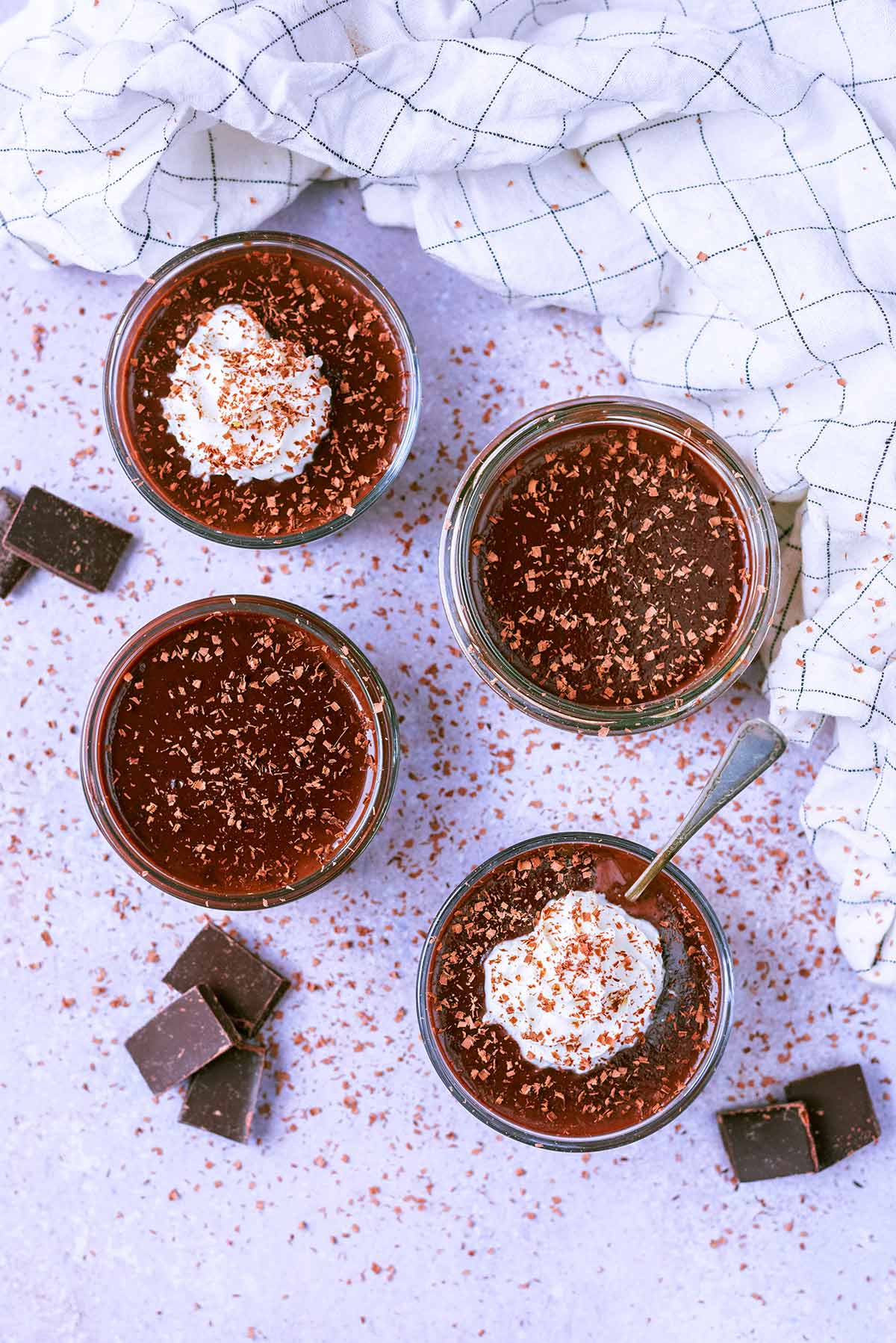 Four glass ramekins each containing a chocolate dessert, two are topped with cream.