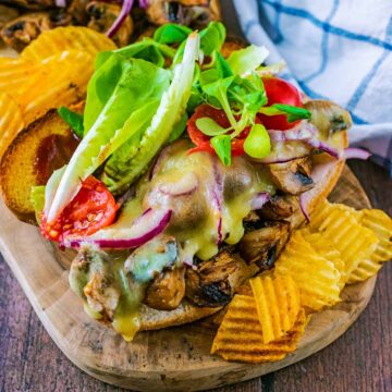 A mushroom sandwich on a wooden board with some crisps.